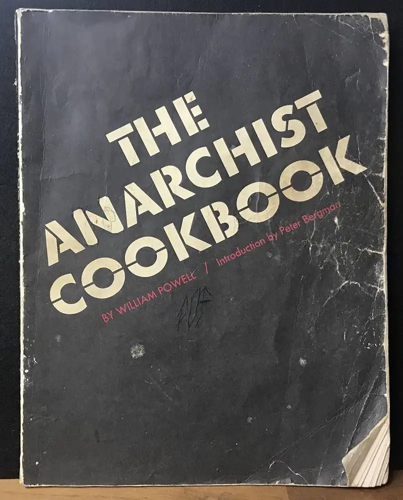 A worn, black-covered book titled 'THE ANARCHIST COOKBOOK' by William Powell with an introduction by Peter Bergman…