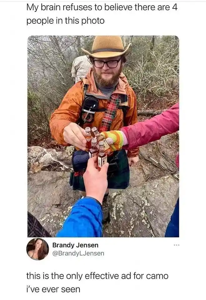 A photo shows a man in an orange jacket, plaid kilt, and tan hat holding several small bottles while standing on a rocky…