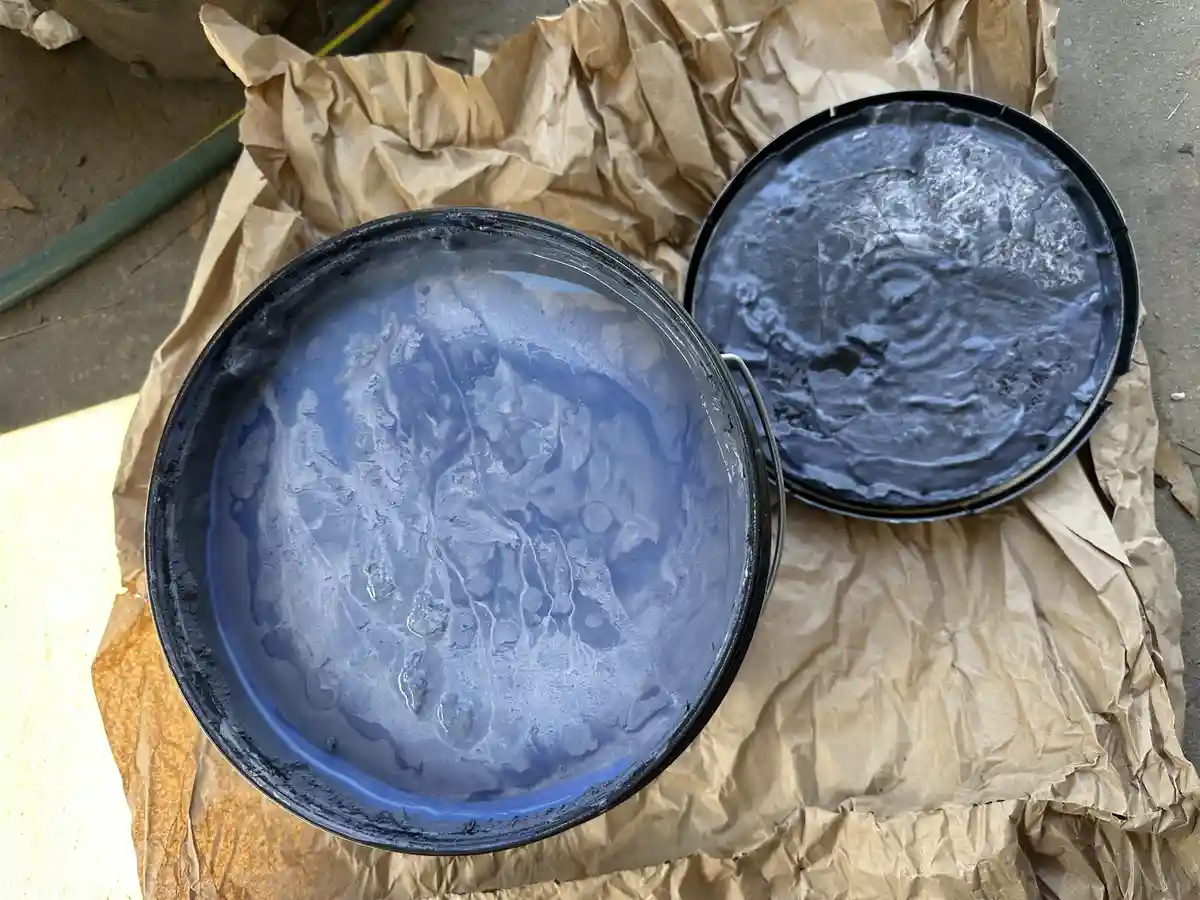 Two open black paint cans sit on crumpled brown paper, their contents frozen solid with visible ice crystals and frost…