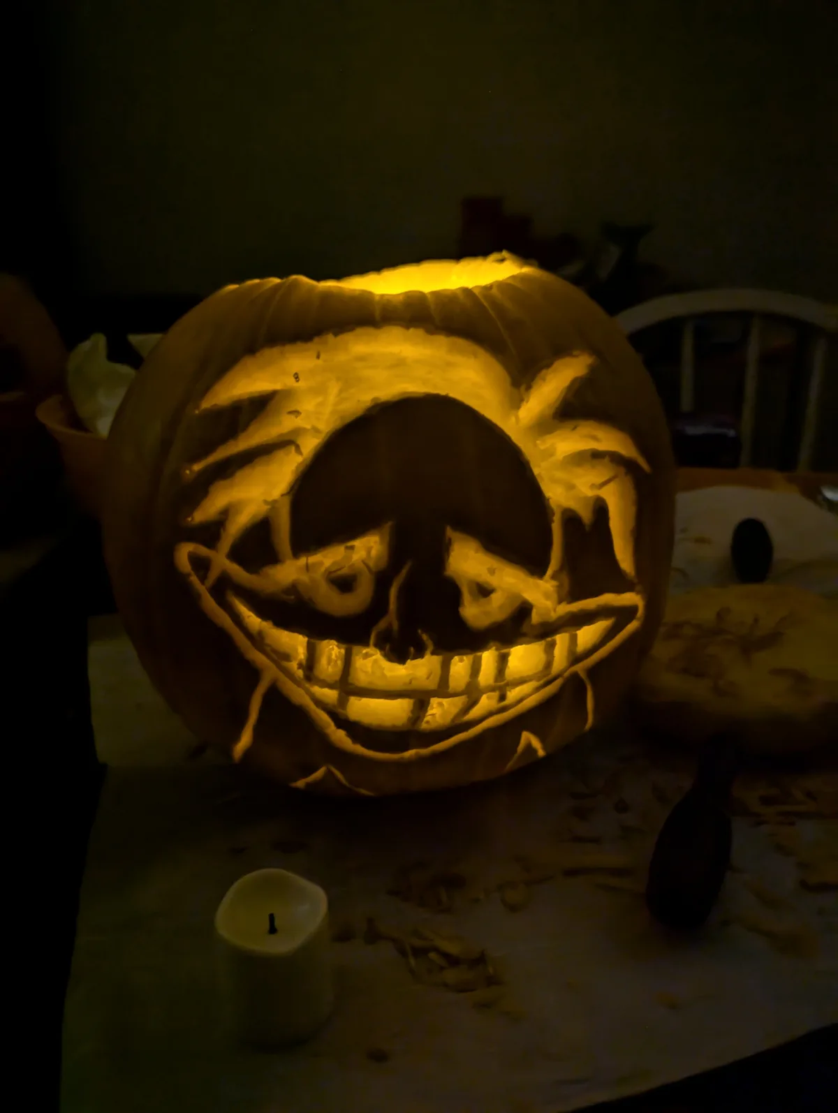 A close-up of a carved Halloween pumpkin illuminated from within, casting a warm glow on its intricate face. The carving…