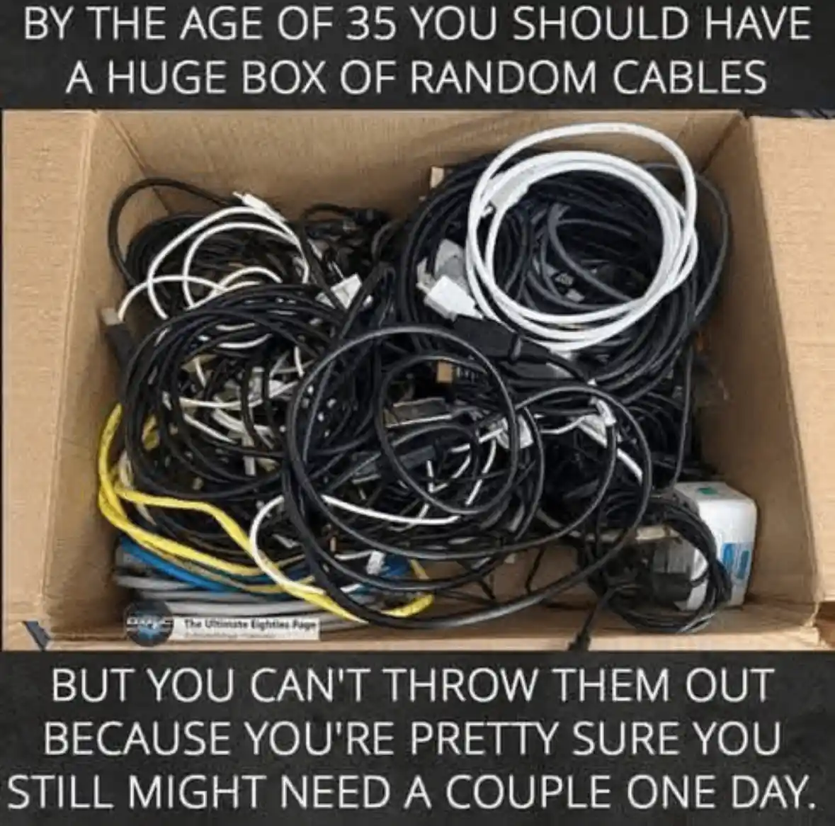 An overhead shot of a cardboard box overflowing with tangled, assorted electronic cables of various colors including black…