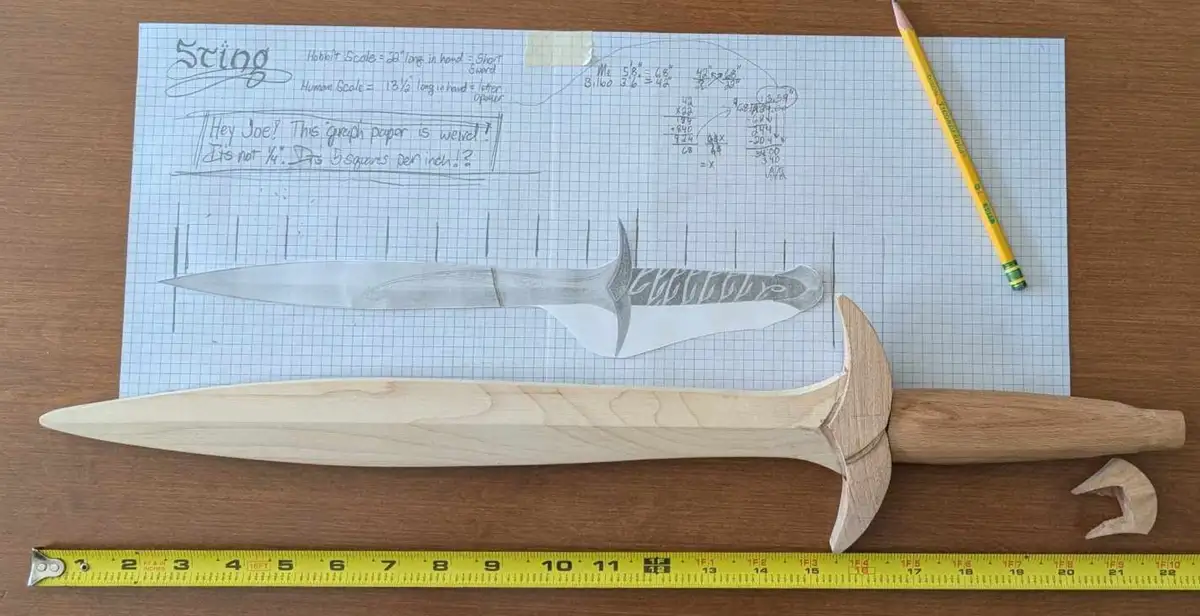 A wooden sword blank lies on a wooden table next to a yellow measuring tape, with a pencil and a detailed pencil sketch of…
