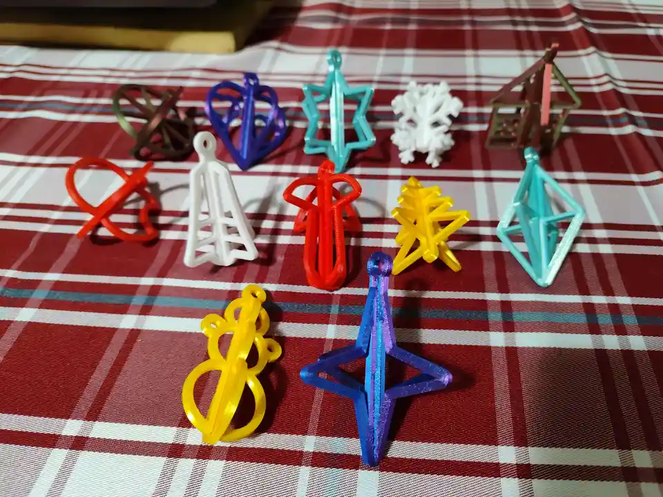 A collection of colorful 3d-printed ornaments, including stars, snowflakes, and abstract shapes, are arranged on a red and…