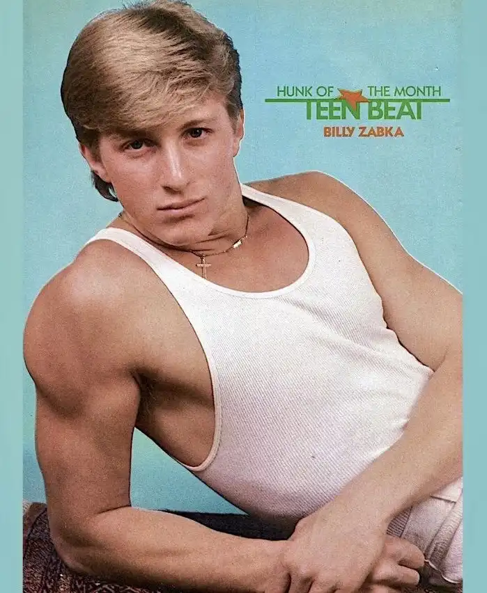 A vintage magazine cover photo shows a young man with styled blonde hair, wearing a white tank top and a cross necklace…