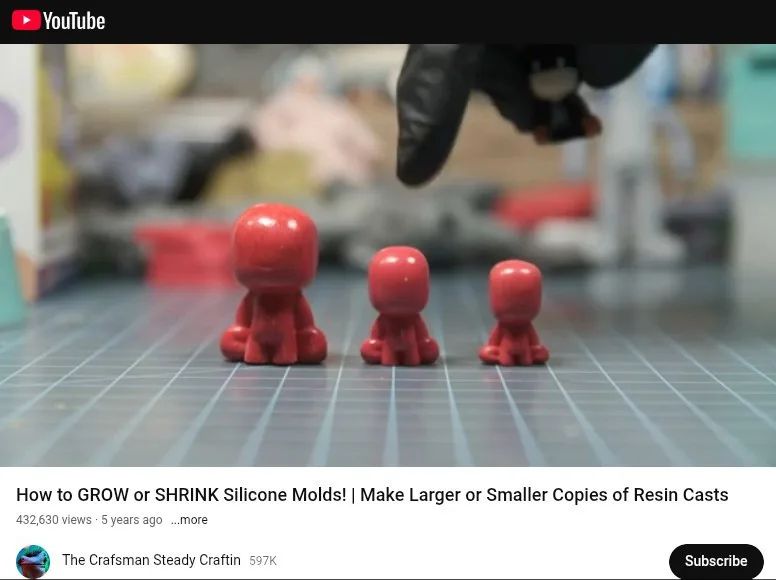 Three red, identical-looking resin figurines sit in a row on a gridded work surface, decreasing in size from left to right…