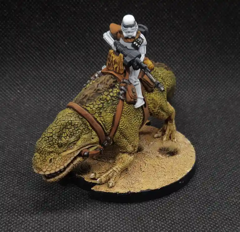 A painted Star Wars miniatures figure shows a stormtrooper in white armor riding a green, scaly bantha. The trooper holds a…
