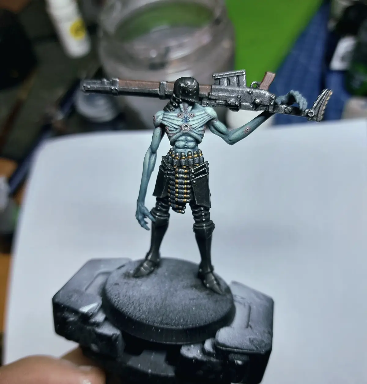 A painted miniature figurine of a blue-skinned, muscular humanoid with a helmet, carrying a large rifle over its shoulder…