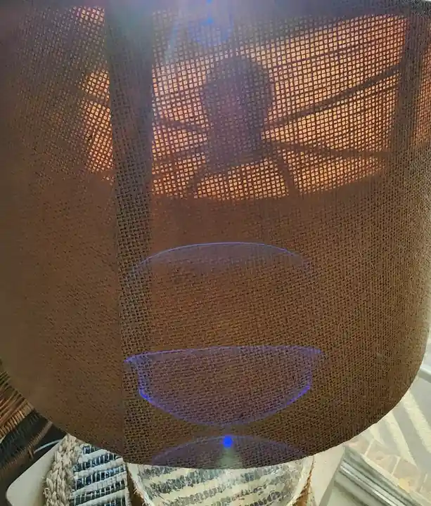 A close-up photo shows a brown, woven-textured lampshade with a blue light glowing faintly from within. The overlaid text…