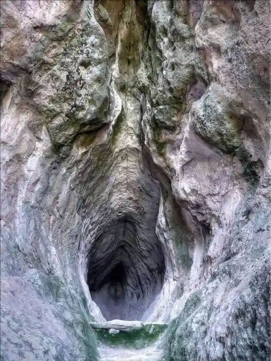 a natural rock formation in a cave entrance resembles a human face with eyes, nose, and mouth carved into the stone…