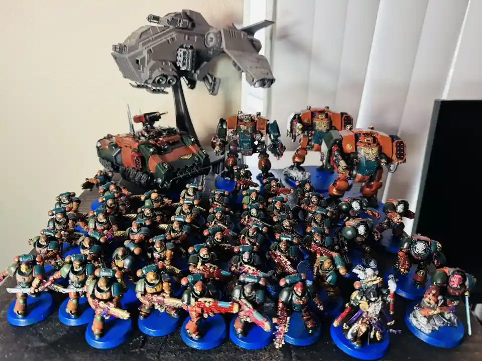 A large collection of painted miniature figurines, mostly in green and orange armor, are arranged on blue circular bases on…