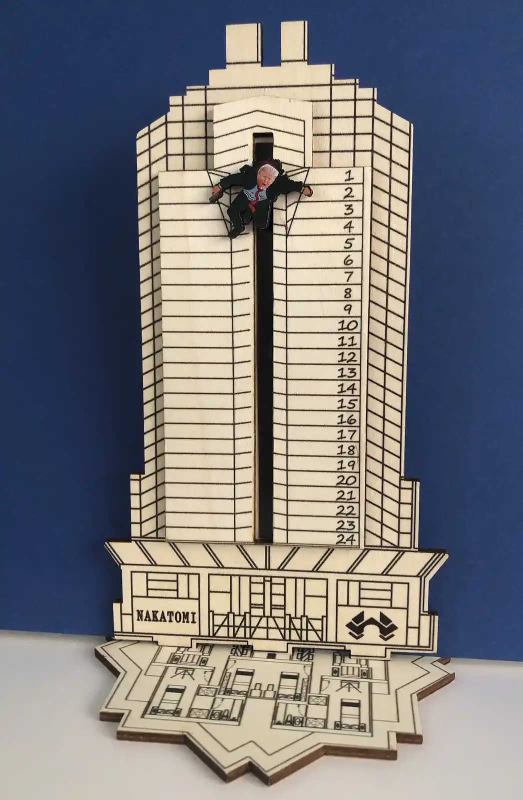 A wooden model of the Nakatomi Plaza building from 'Die Hard' with a cutout of Donald Trump's face glued to a figure…