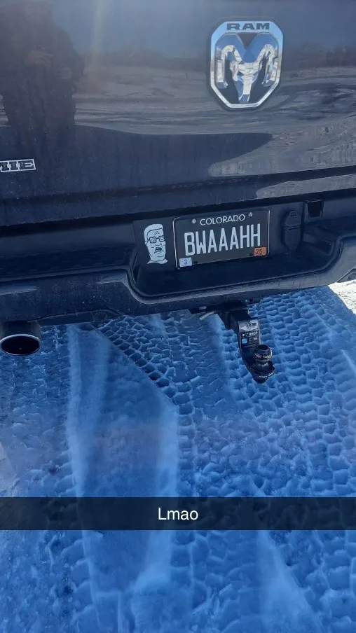 The rear of a black Ram truck is shown parked on a snowy surface, with a Colorado license plate reading 'BWAAAH' and a…