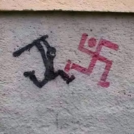 A rough, black spray-painted figure resembling a person running or falling is drawn next to a red swastika symbol on a…