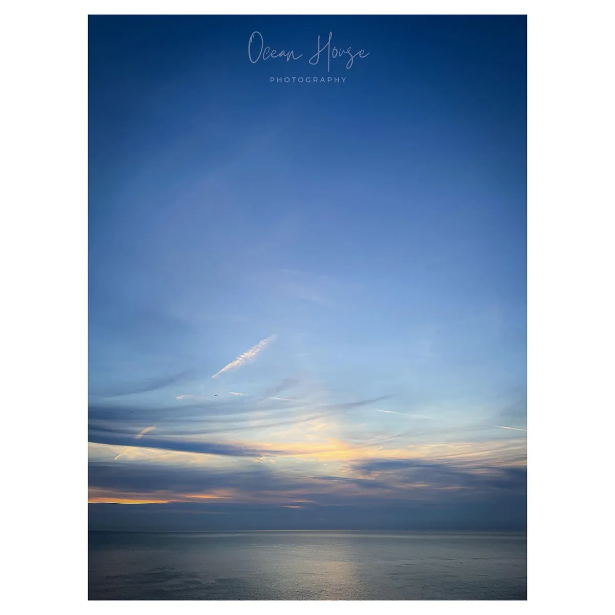 A serene photograph of a calm ocean at sunset or sunrise, with a gradient sky transitioning from deep blue to soft orange…