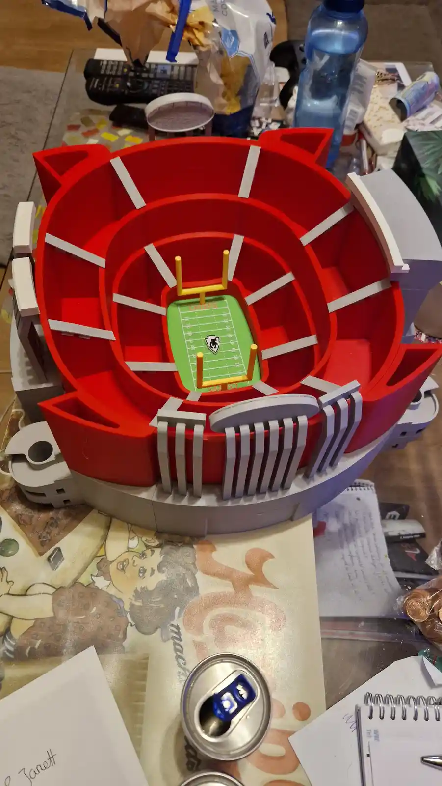 A top-down view of a red plastic toy stadium model with a green football field marked with yard lines and the word 'CHIEFS'…