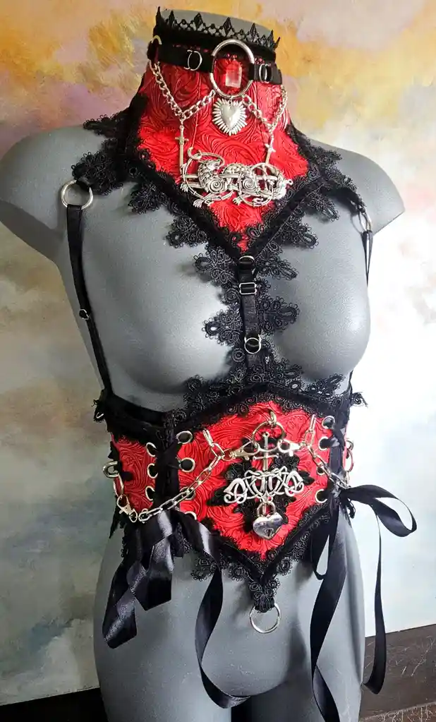 A gray mannequin displays an elaborate red and black lingerie set with lace, chains, metal rings, and ornate silver charms…