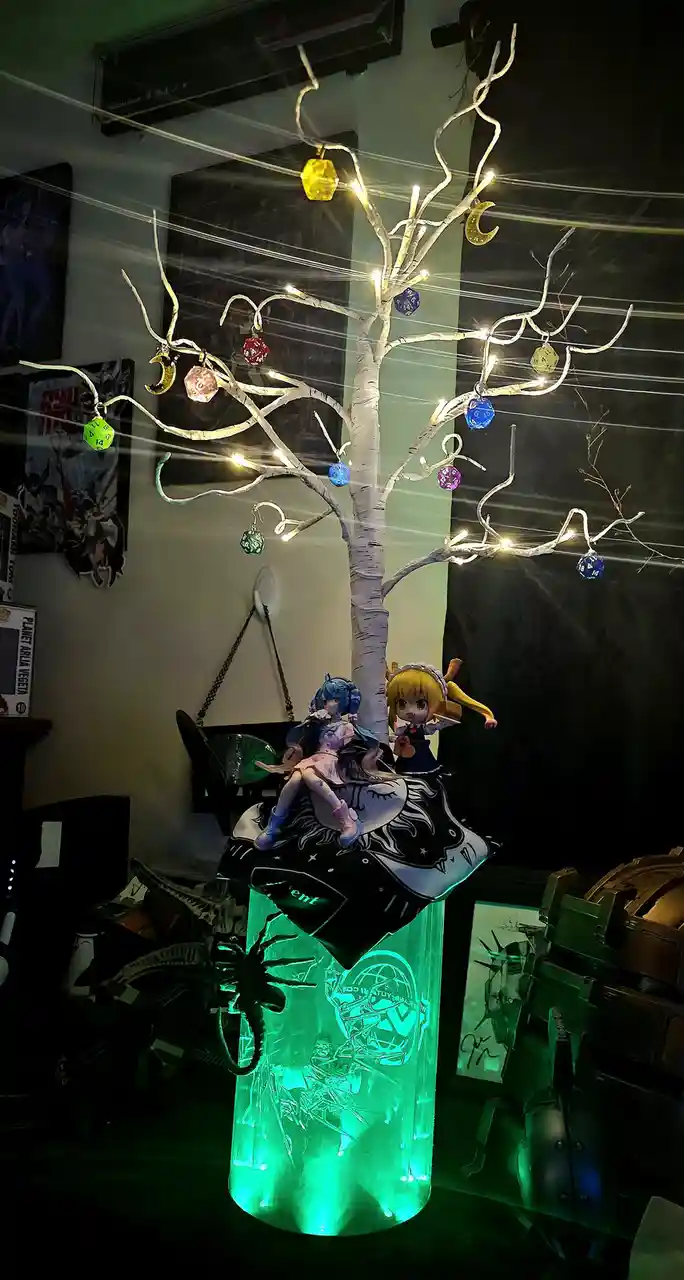 A decorative white birch-style tree with string lights and colorful polyhedral dice ornaments hangs in a dimly lit room. Two…