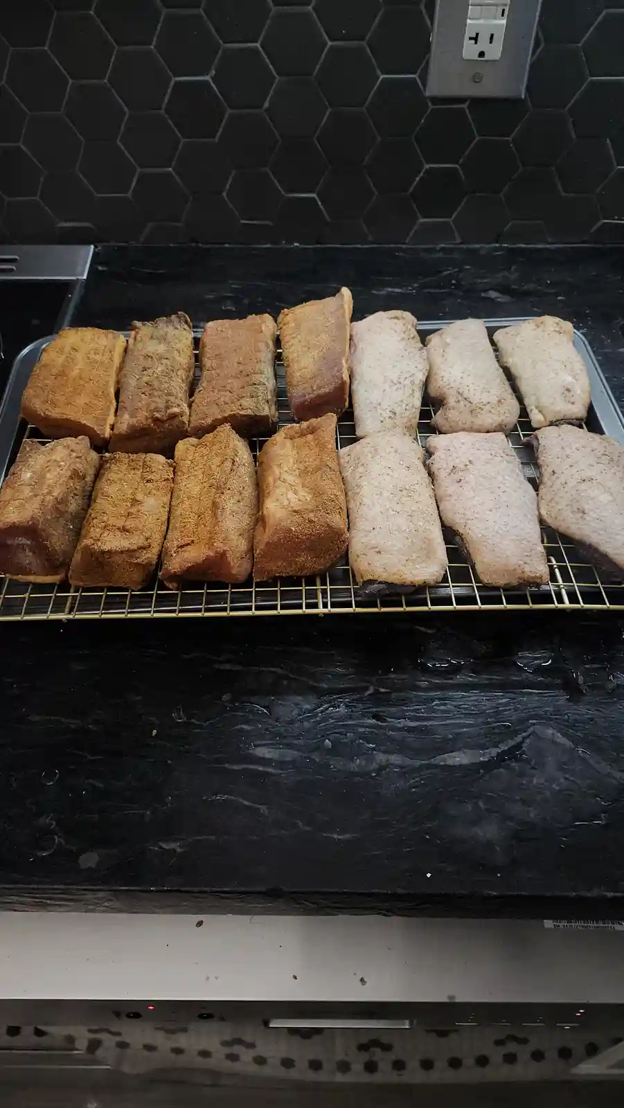 A metal baking rack holds two rows of meatloaf-like pieces; the left row is browned and cooked, while the right row is pale…