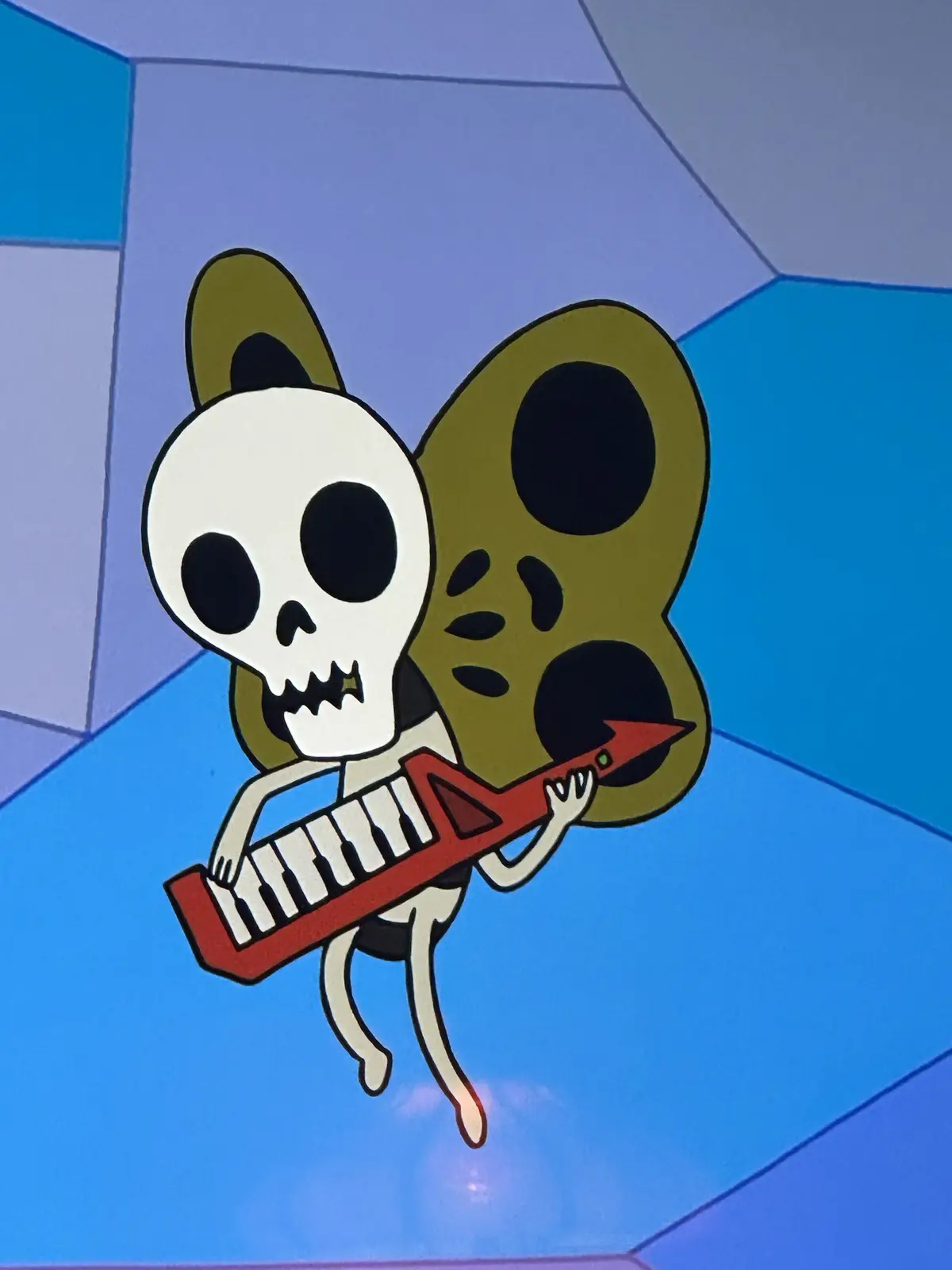 A cartoon skeleton with large green butterfly wings is floating against a blue geometric background while playing a red…