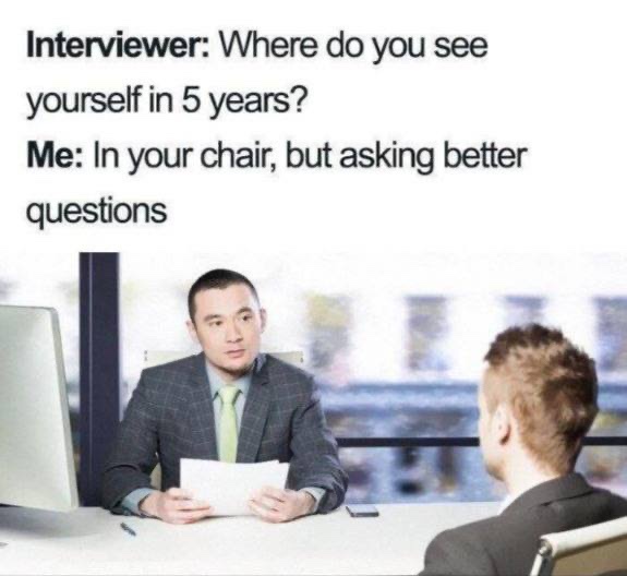 An image shows two men in a job interview setting, one facing the camera as the interviewer holding papers, the other seen…