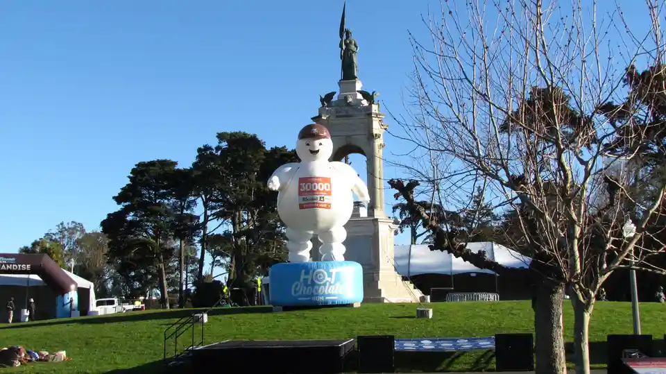A large inflatable marshmallow man wearing a race bib with the number 30000 stands on a blue base labeled 'HOT Chocolate…