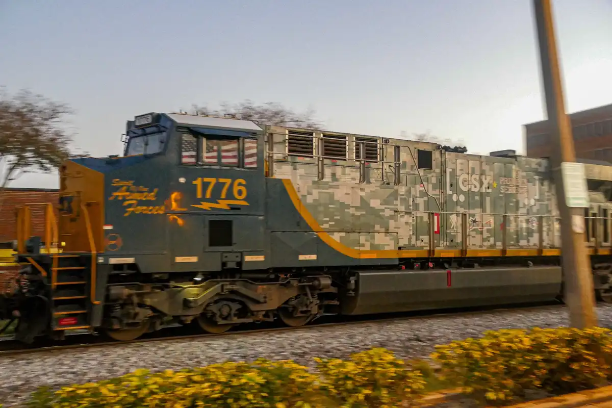 A CSX locomotive, number 1776, is shown in motion with a military camouflage paint scheme and 'Salute to the Armed Forces'…