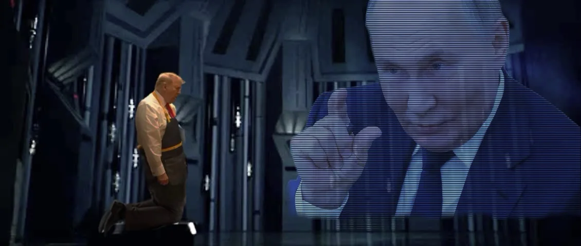 A man in a white shirt and apron kneels on a dark floor facing a large screen displaying a man in a suit pointing directly…