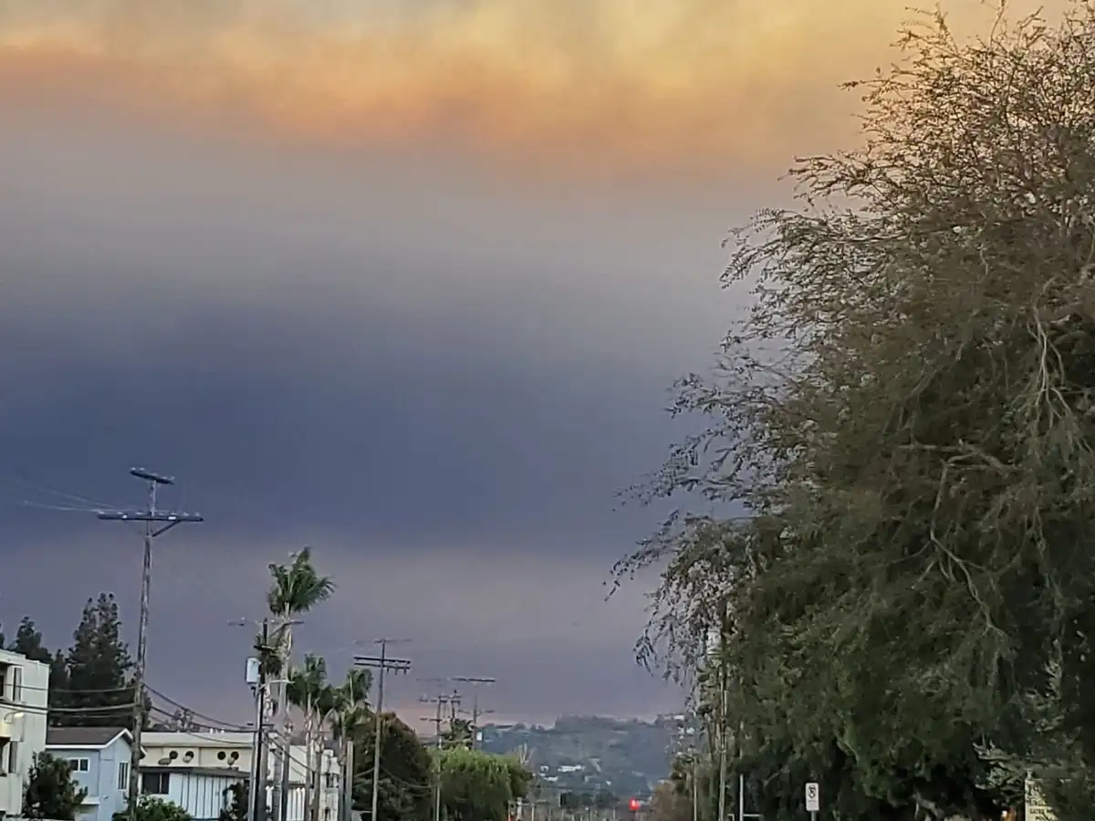 A street view shows a dramatic sky with a lower layer of dark gray clouds and a fiery orange-yellow haze above, suggesting…
