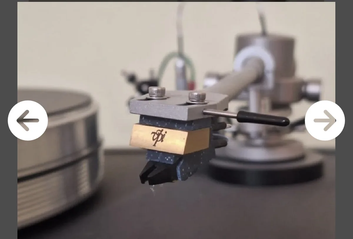 A close-up photo of a high-end turntable cartridge with a brass plate engraved with the Greek letter pi (π), set against a…
