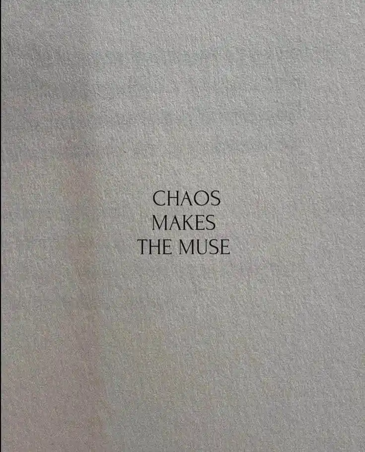 The image shows plain, textured gray paper with the text 'CHAOS MAKES THE MUSE' centered in a simple black serif font. The…