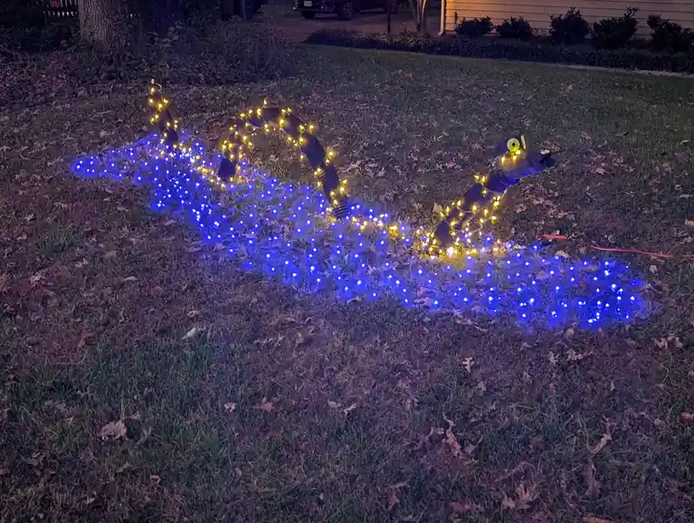 A nighttime photo of a lawn decorated with string lights forming the shape of a dragon, with blue lights outlining the body…