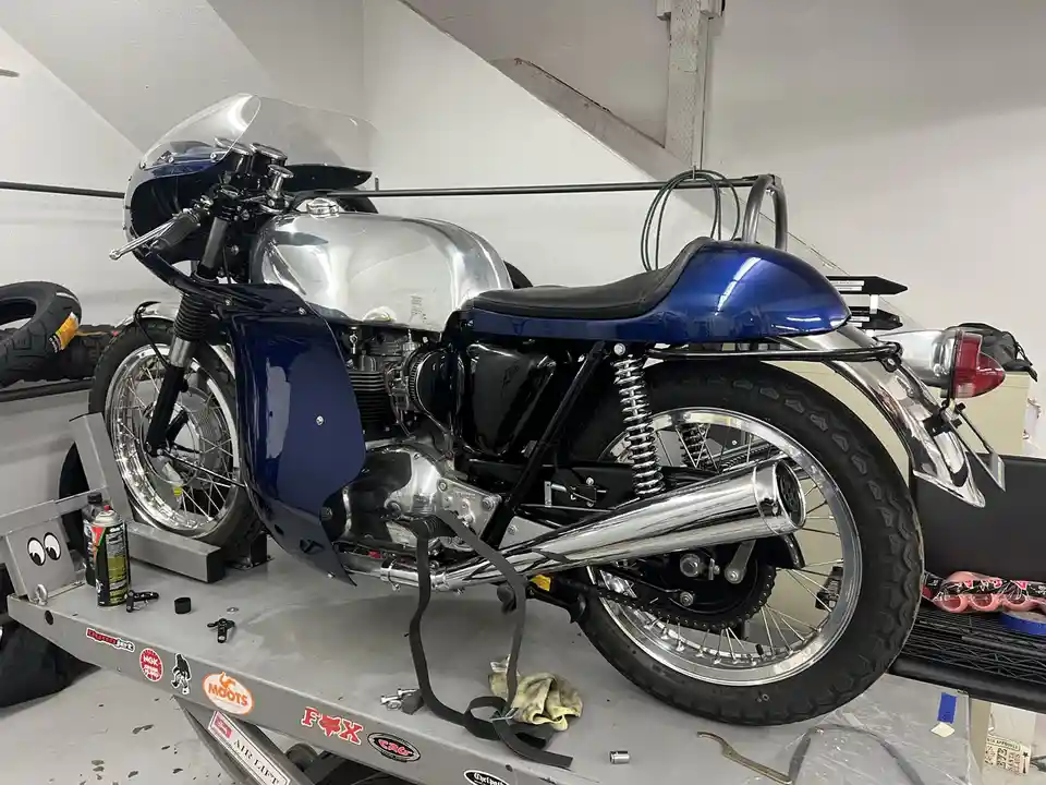 A custom blue and chrome motorcycle is parked on a hydraulic lift in a garage, surrounded by tools and parts. The bike has a…
