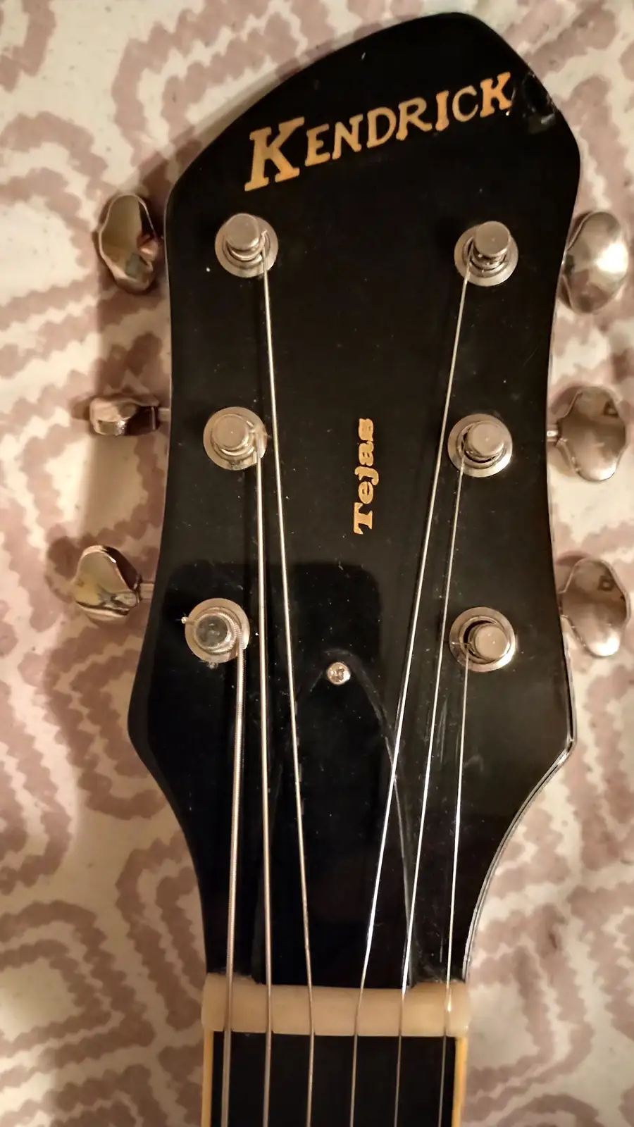 A close-up photo of a black guitar headstock with the brand name 'KENDRICK' in gold lettering at the top and 'Tejas' below…