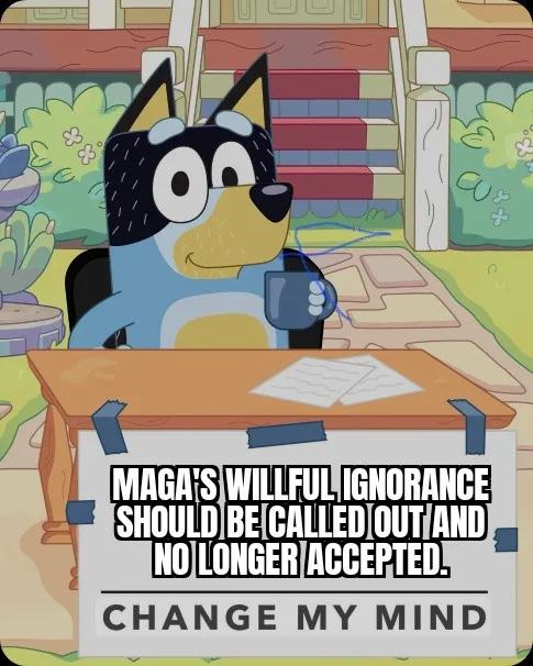 A cartoon blue dog with large eyes sits at a wooden desk holding a mug, with a white sign taped to the desk that reads…
