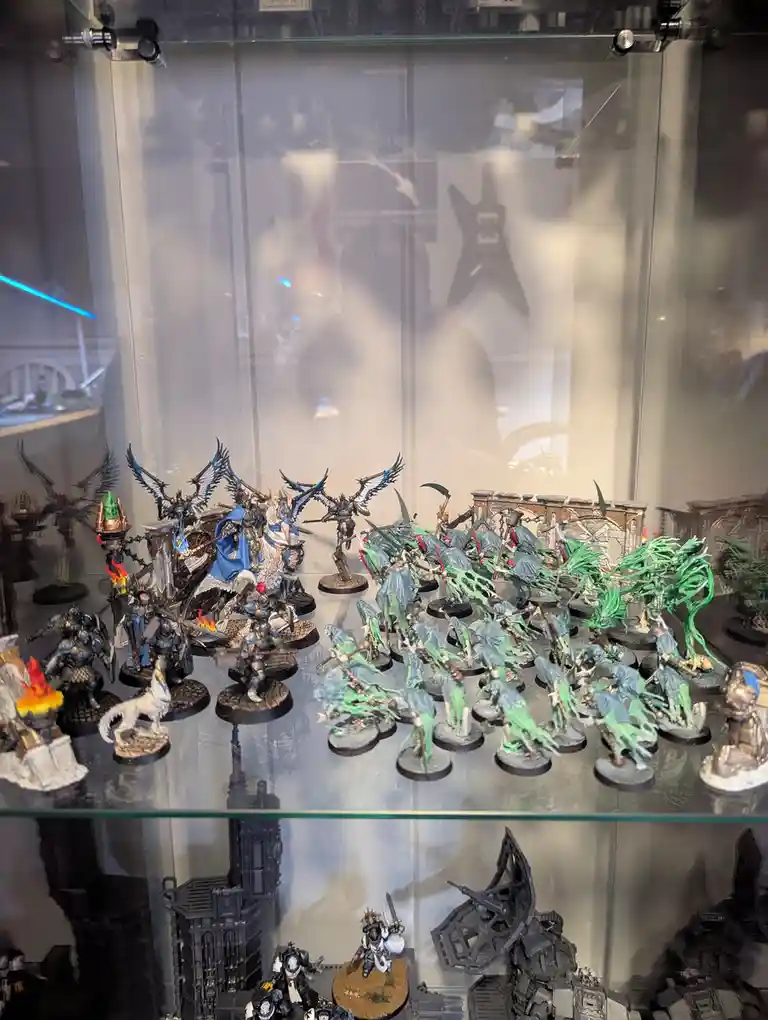 A glass display case holds numerous painted miniature figurines, including a large group of green-skinned, tentacled…