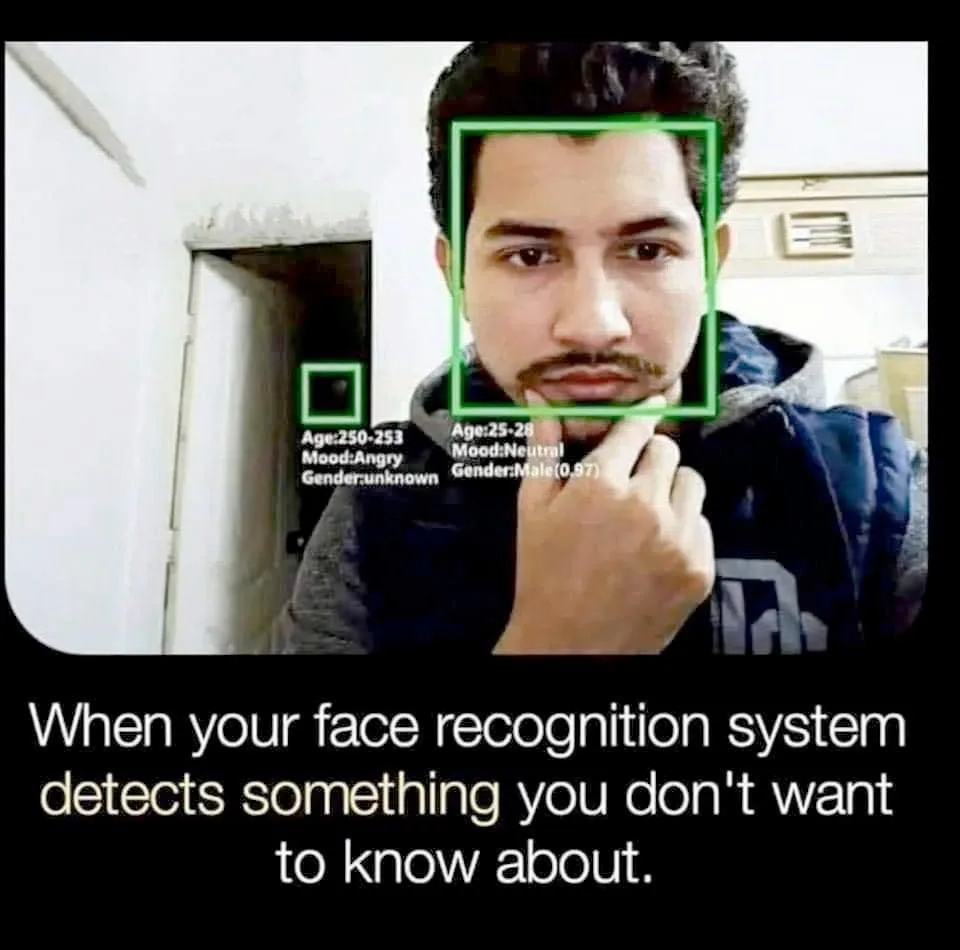 A man with a mustache and dark hair looks at the camera with a neutral expression while touching his chin. A green facial…