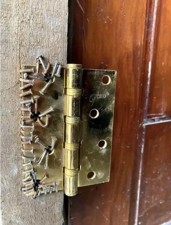 A close-up photo shows a brass door hinge with multiple screws visibly protruding from its edge, appearing to be nailed or…