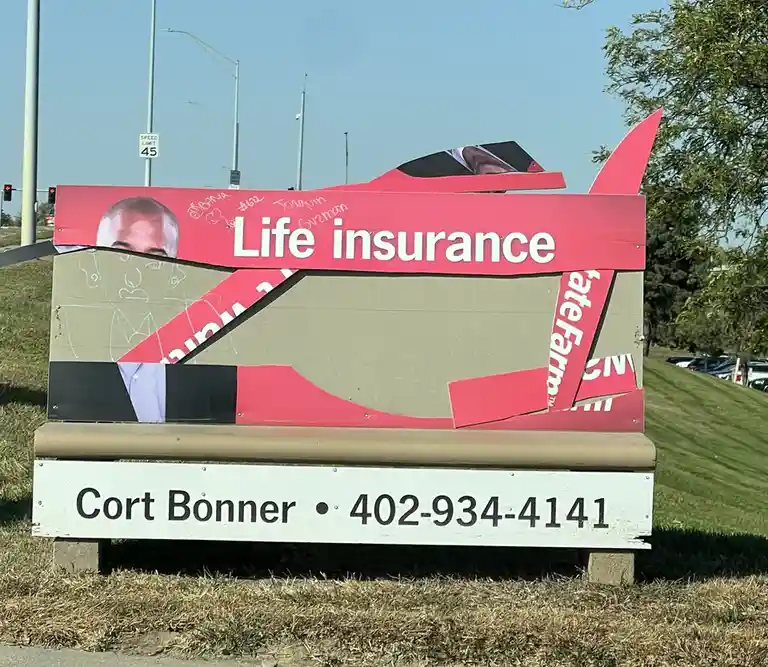 A heavily damaged and torn life insurance sign for Cort Bonner, with pieces of the red and beige panels ripped away…