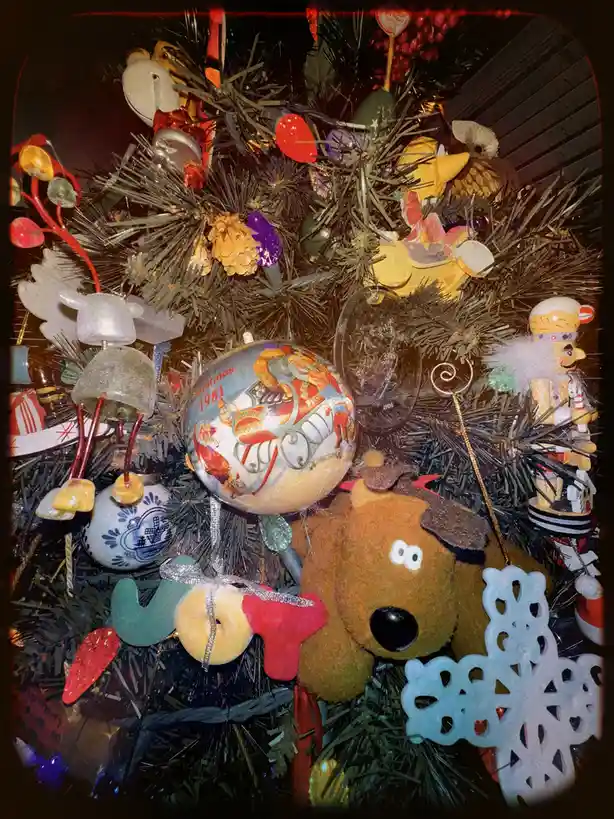 A close-up of a densely decorated artificial Christmas tree with numerous vintage ornaments, including a prominent glass…