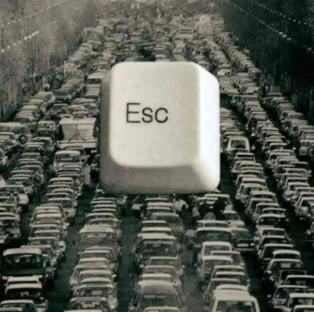 A black-and-white photo shows a massive computer keyboard 'Esc' key hovering over a dense, grid-like traffic jam of vintage…