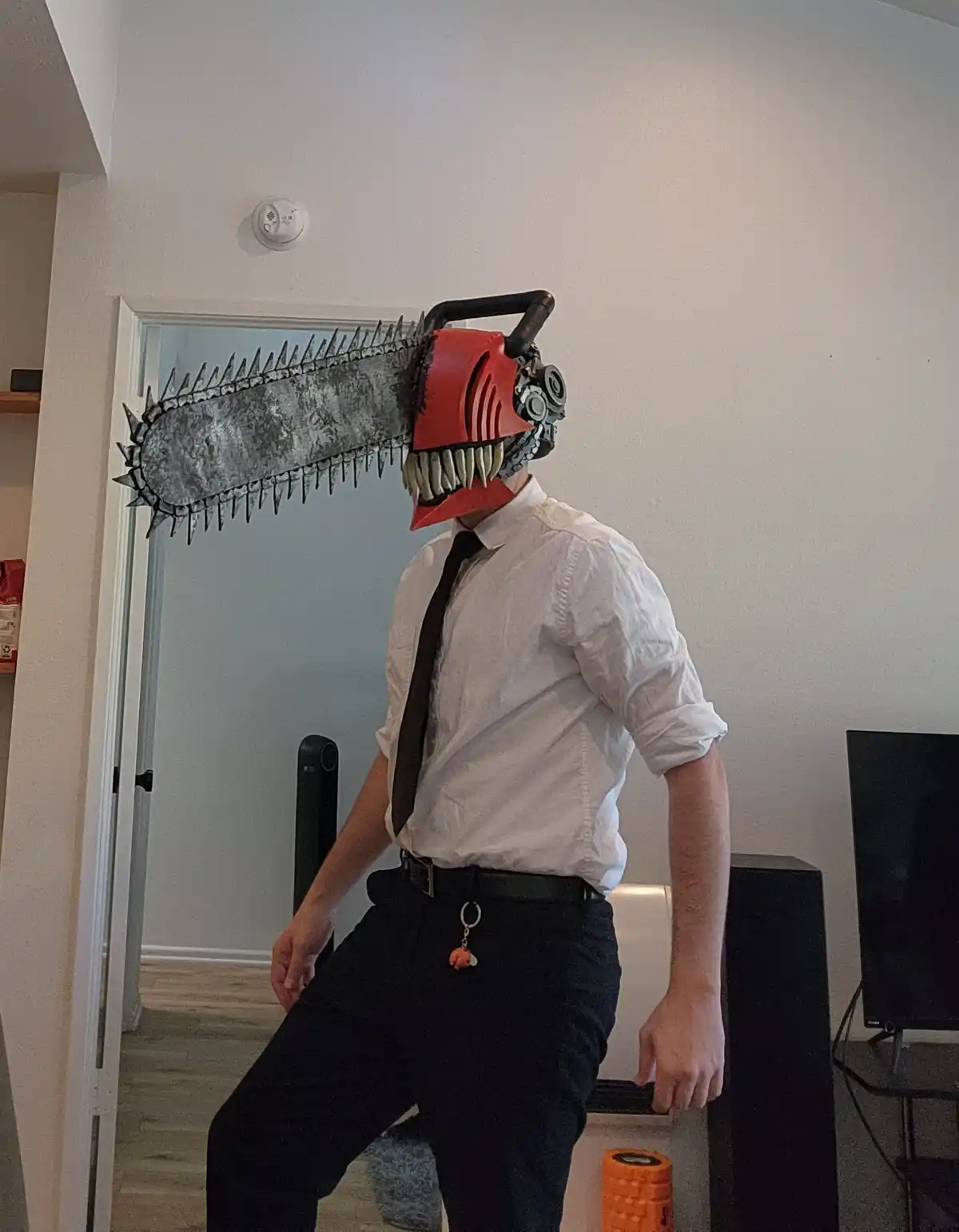 A person wearing a chainsaw mask with teeth and a red body, dressed in a white button-down shirt, black tie, and black…