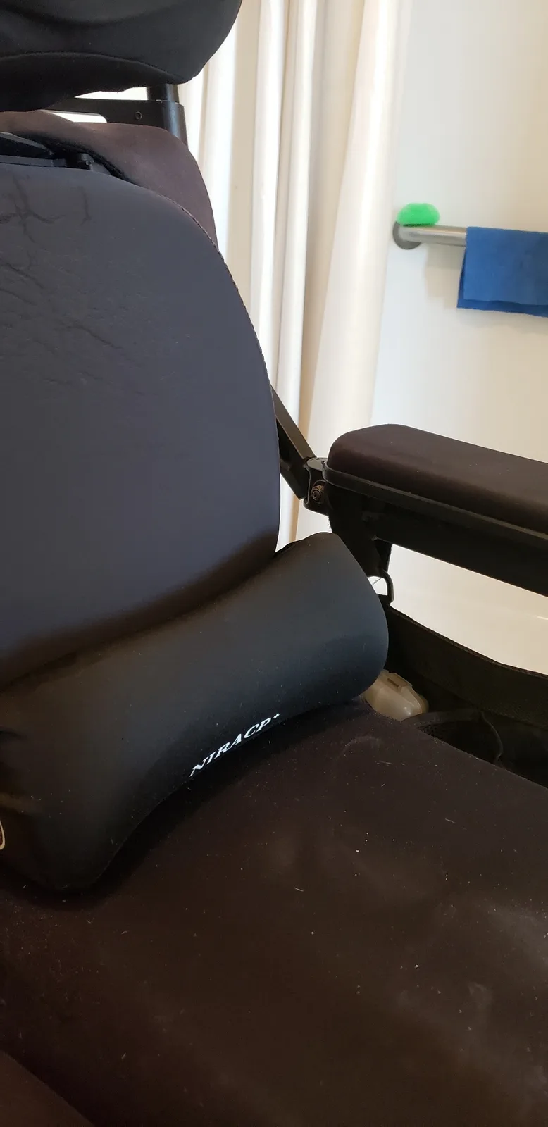 A close-up photo shows a black, contoured neck pillow with the brand name 'NIRACP+' printed in white on its side, resting on…
