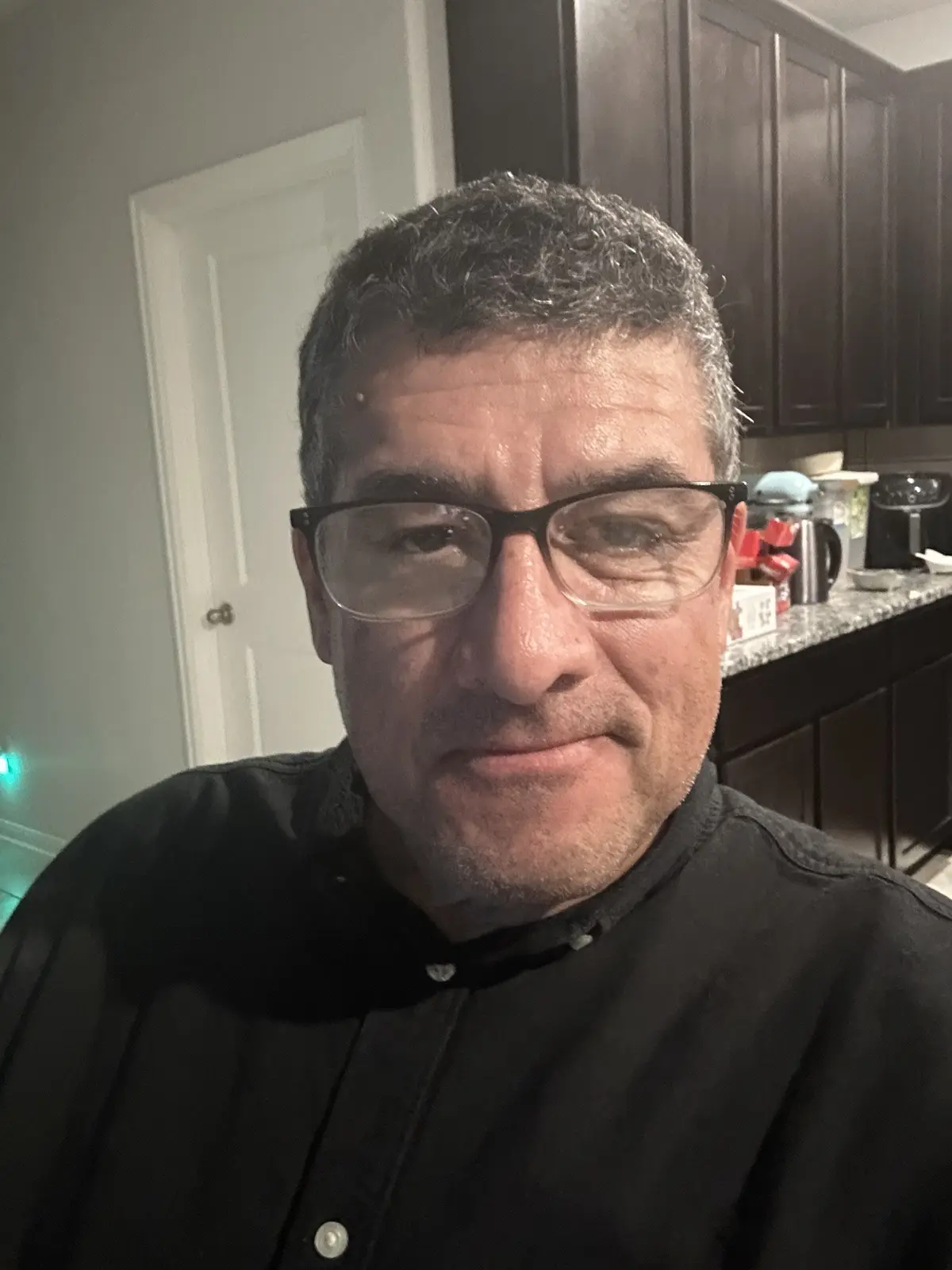 A man with graying hair and black-rimmed glasses stares directly at the camera with a subtle, slightly smug expression. He…