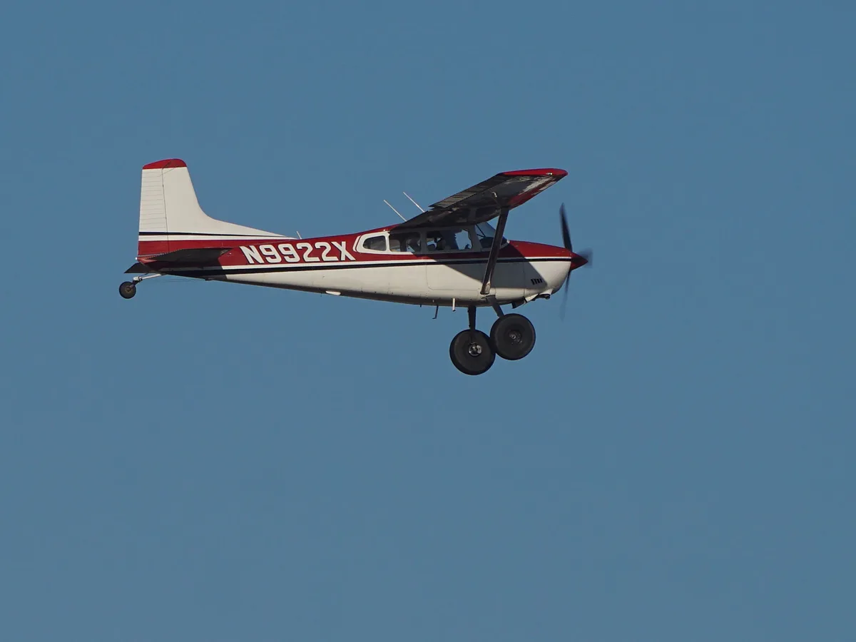 A red and white single-engine propeller airplane with the registration number N9922X is flying against a clear blue sky, its…